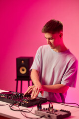 Young DJ with headphones, Skilled DJ engaging with equipment in lively environment, Energetic DJ prepping for live performance amid colorful lighting and fashionable attire