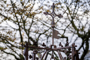 Ornate metal cross and banner finial against tree branches at a historic abbey. Decorative wrought-iron weather vane with gothic details at Mont Saint-Michel. 