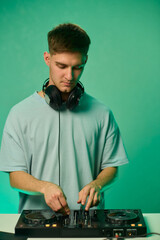 Young DJ with headphones, Skilled DJ engaging with equipment in lively environment, Energetic DJ prepping for live performance amid colorful lighting and fashionable attire