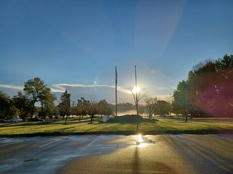 A beautiful morning sunrise over an open field at the edge of a parking lot with scattered trees.