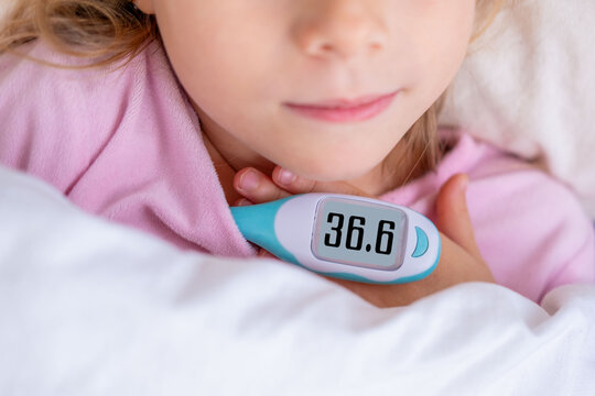 Child in pink pajamas holds digital thermometer showing 36.6 C, smiling under white blanket, healthy temperature, home care, and parental reassurance during wellness check