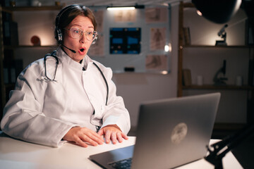 Shocked Female doctor in uniform wear headset has omg emotions use laptop computer talking on video...