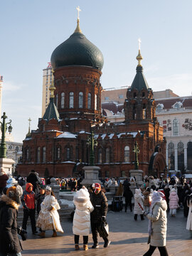Harbin, China - 23 December 2023: View of the magnificent, red-brick St. Sophia Cathedral stands as a testament to history, framed by a lively crowd under a clear, crisp winter sky.