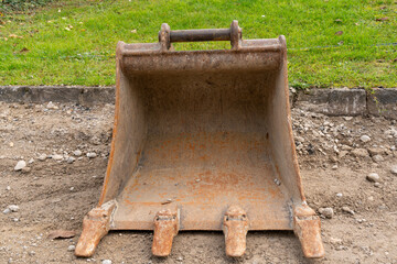 Closeup on rusty excavator bucket on the ground, looking into the bucket. Construction site. Green meadow in the background.