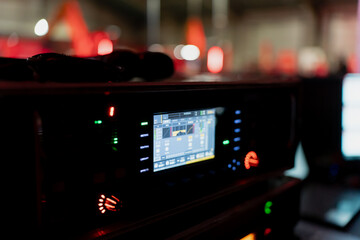 Stage rack device featuring colorful monitoring screen, signal levels and illuminated buttons captured in low light production workspace with soft bokeh lights
