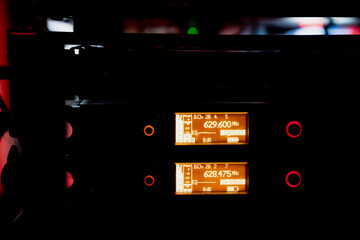 Close view of paired electronic measurement screens embedded in an equipment rack, each displaying bright frequency readouts and small status icons inside a low-light technical workspace