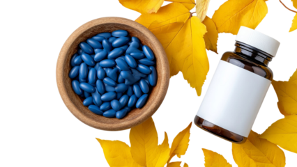 PNG of A wooden bowl filled with blue capsules beside a white-labeled bottle, surrounded by vibrant autumn leaves.