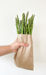 a woman's hand holds fresh asparagus in a paper bag