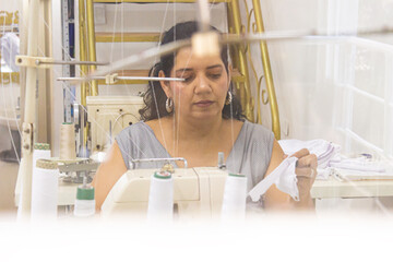 Portrait of a Colombian fashion designer creating dresses from fabric on a sewing machine in a...