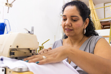 Portrait of a Latina dressmaker working on a sewing machine creating dresses in a fashion workshop...