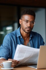 Obraz premium African male adult reading newspaper at cafe with laptop and coffee