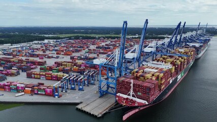 Aerial drone view of container ship docked at busy shipping port with cranes - Powered by Adobe