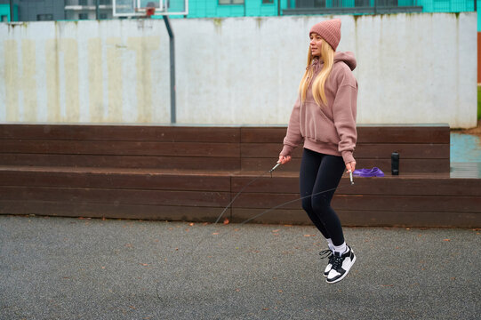 Young woman exercising outdoors with jump rope on court