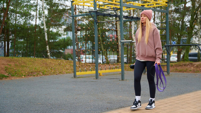 Woman standing at outdoor gym with jump rope and water bottle