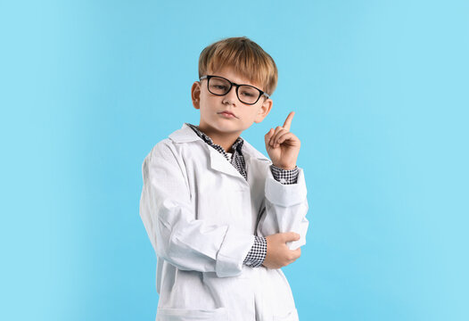 Thoughtful little boy in laboratory coat and glasses on light blue background. Child and science