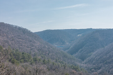 A broad, hazy view of a steep, wooded valley Dolina Glin ice in the Karst region, with a massive concrete bridge viaduct visible in the distant center.