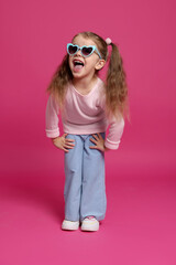 Naklejka premium Emotional little girl in sunglasses on pink background