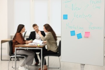 Fototapeta premium Colleagues discussing strategy in office, focus on whiteboard with business plan scheme and sticky notes