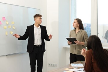 Man giving presentation for his colleagues near whiteboard with sticky notes in office
