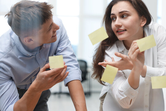 Colleagues discussing strategy near glass board sticky notes in office