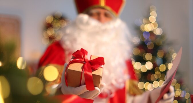 Saint Nicholas with gift and letter at desk in room decorated for Christmas, selective focus