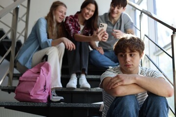 Students bullying their classmate on stairs indoors, selective focus