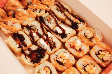 A close view of assorted fried sushi rolls arranged in a delivery box, topped with sauces and crispy textures. The image highlights variety, richness, and modern takeaway cuisine
