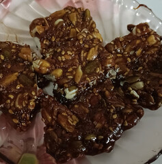 Dark, glossy mixed-seed and nut chikki pieces made with jaggery syrup. The brittle features pumpkin...