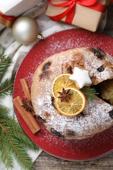 Tasty Christmas panettone cake with powdered sugar and festive decor on wooden table, flat lay