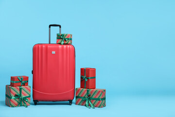 Christmas vacation. Red suitcase and gift boxes on light blue background. Space for text