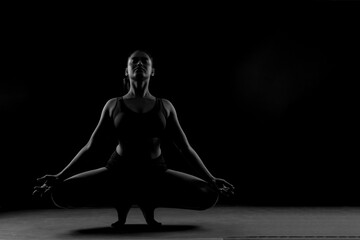 Dramatic silhouette of a woman performing an yoga . Artistic black and white studio fitness photography with rim lighting.