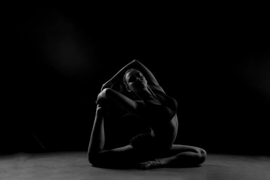 Dramatic silhouette of a woman performing an yoga . Artistic black and white studio fitness photography with rim lighting.