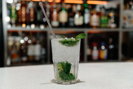 mojito cocktail in glass with mint and ice cubes and straw on bar counter, nightlife concept