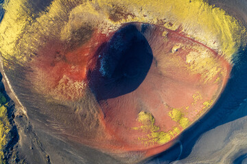 Aerial view of a volcanic crater's dark heart, ringed by fiery red and gold hues, contrasting against the stark Icelandic landscape, Akureyri, Rangarbing ytra, Iceland.
