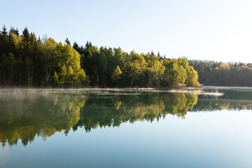 Obraz premium Mirror-Smooth Lake Reflects Serene Forest on Sunny Day for Peaceful Nature Scene.