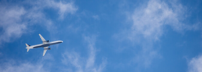 Commercial airplane flying above light clouds with clear view of the aircraft underside against a bright blue sky