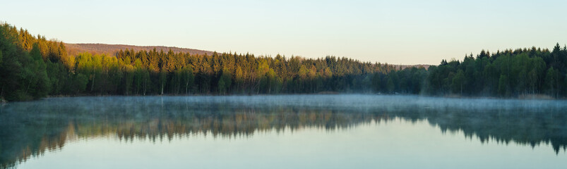 Mirror-Smooth Lake Reflects Serene Forest on Sunny Day for Peaceful Nature Scene.