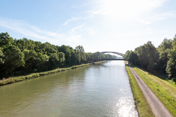 Fototapeta premium Tranquil Water Canal Winding Through Green Landscape Under Blue Summer Sky.