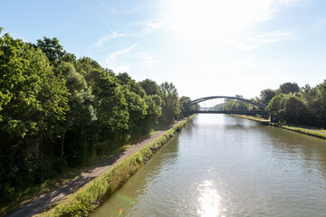 Fototapeta premium Tranquil Water Canal Winding Through Green Landscape Under Blue Summer Sky.