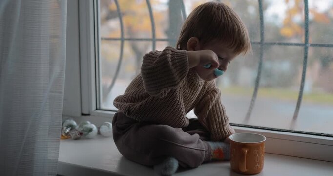 A little boy drinking tea sitting on the windowsill at the autumn day. Video contains original audio.