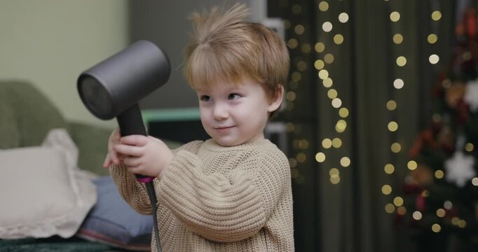 A little boy blow-dries his hair at home, slow motion