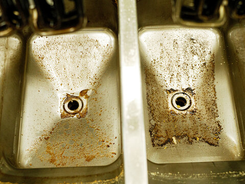 Dirty stainless steel deep fryer sections with heavy cooking residue and oil stains in professional restaurant kitchen before cleaning and maintenance