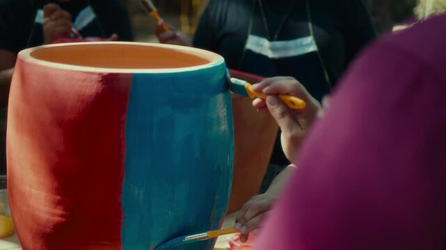 Real video of people painting a handcrafted drum with brushes, applying blue and red paint on the surface. The shot highlights the creative process