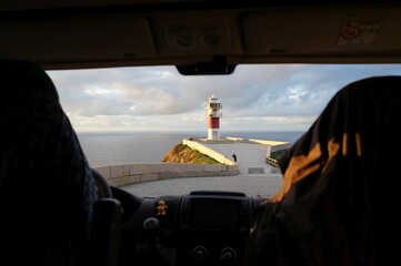 Fototapeta premium Lighthouse in Spain at sunset viewed from the inside of a campervan with the sea in the background