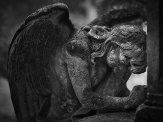 Weathered stone angel in a mourning pose at Goat Gate Cemetery in Bratislava, photographed in black and white.