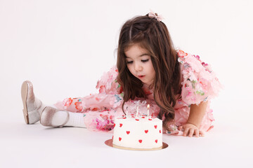 Birthday celebration. Cute little girl in dress blowing out candles on tasty cake on white background