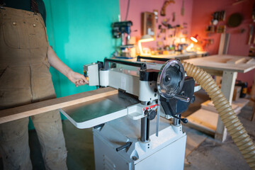 Closeup of carpenter shaping wooden block on planer thicknesser jointer machine in workshop. Woodworking process, furniture preparation, handmade craftsmanship, precision tools, carpentry studio