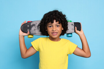 Portrait of little boy with penny board on light blue background