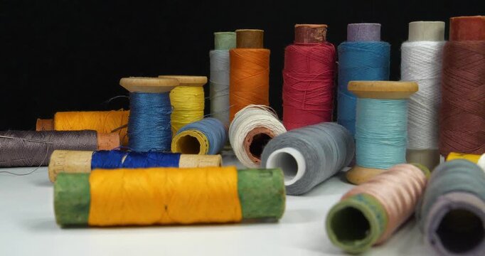 Beautiful multi-colored spools of thread lie on white table and rotates on black background