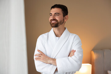 Handsome man wearing comfortable white bathrobe indoors